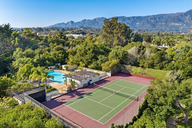 view of tennis court featuring a forest view, fence, and a mountain view