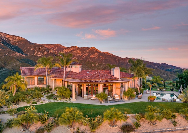 back house at dusk with a yard, a mountain view, and a patio area