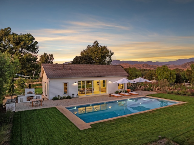 back house at dusk with a yard, a mountain view, an outbuilding, and a fenced in pool