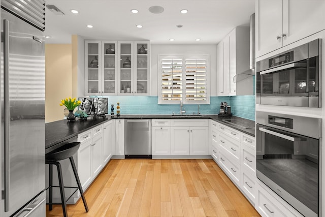 kitchen featuring light wood-type flooring, tasteful backsplash, stainless steel appliances, sink, and white cabinetry