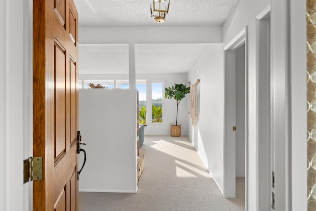 hall with light colored carpet and a textured ceiling