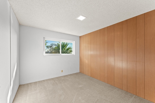 unfurnished room with wood walls, a textured ceiling, and light carpet