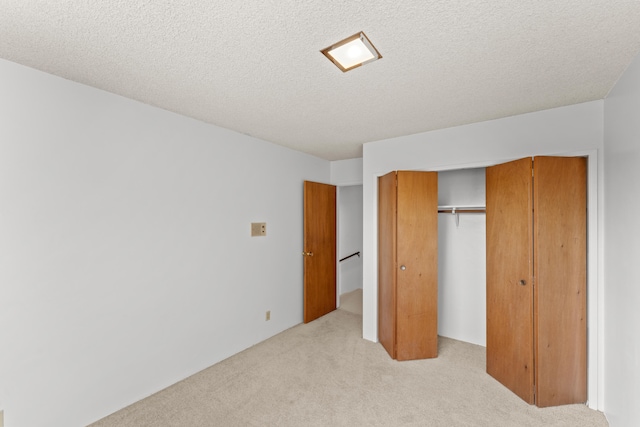 unfurnished bedroom featuring light colored carpet, a textured ceiling, and a closet