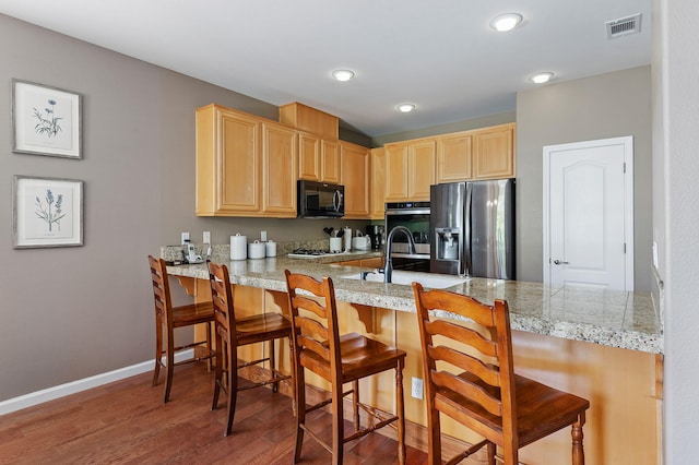 kitchen featuring hardwood / wood-style flooring, a breakfast bar, kitchen peninsula, appliances with stainless steel finishes, and light brown cabinets