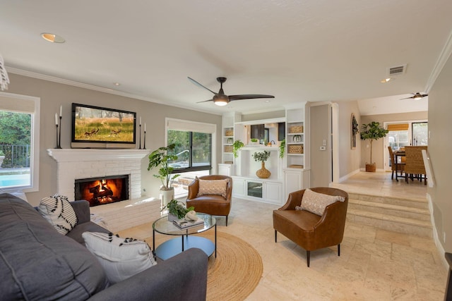 living room with a fireplace, ceiling fan, a healthy amount of sunlight, and crown molding