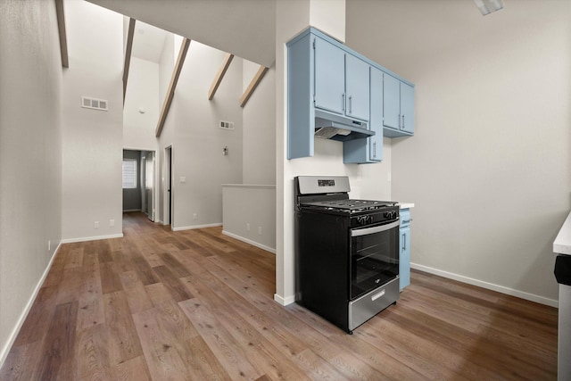 kitchen featuring stainless steel range with gas cooktop, blue cabinetry, a high ceiling, and light hardwood / wood-style floors