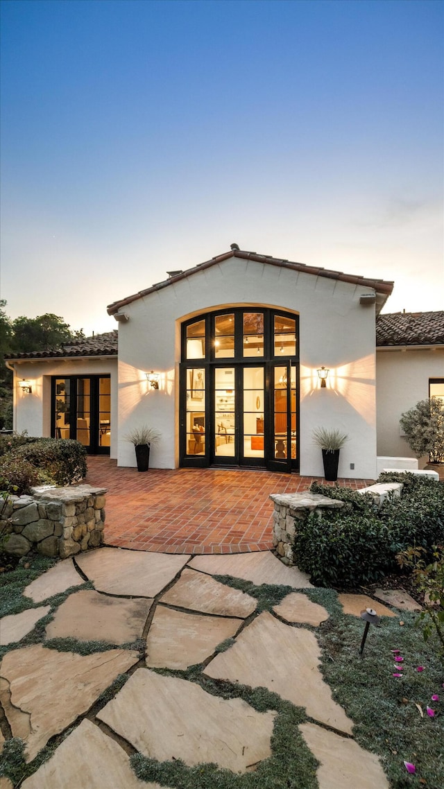 back house at dusk featuring a patio and french doors