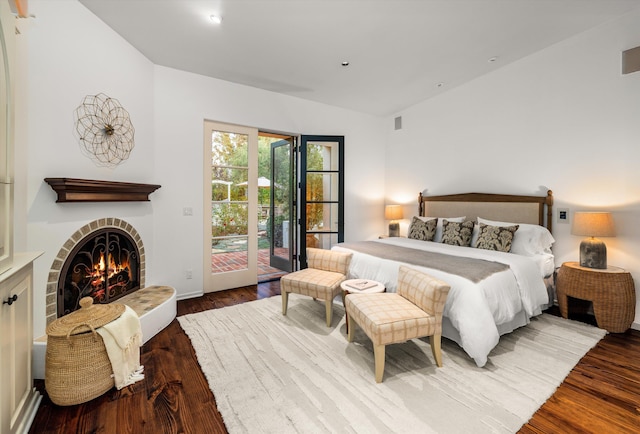 bedroom featuring access to outside, hardwood / wood-style floors, lofted ceiling, and a brick fireplace