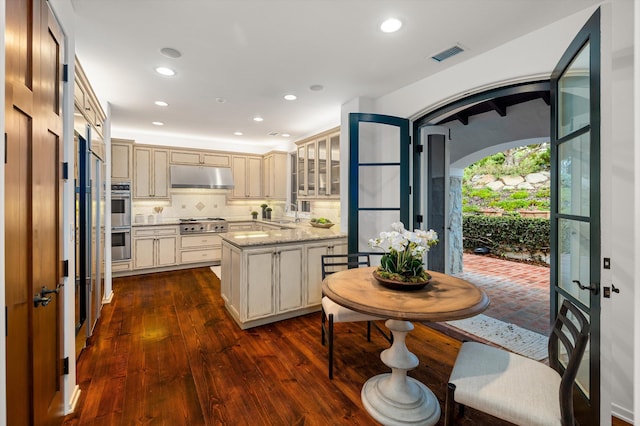 kitchen with dark wood-type flooring, tasteful backsplash, light stone counters, cream cabinets, and a kitchen island