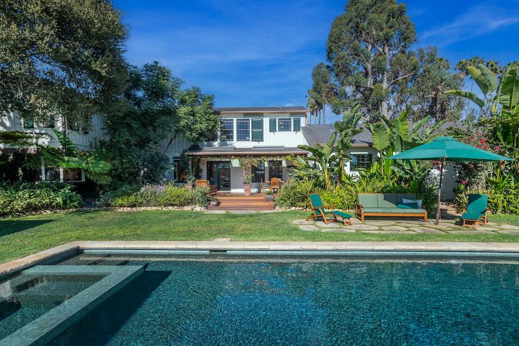 rear view of house featuring a pool with hot tub and a yard