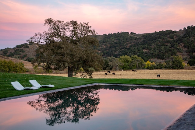 pool at dusk featuring a yard and a water view