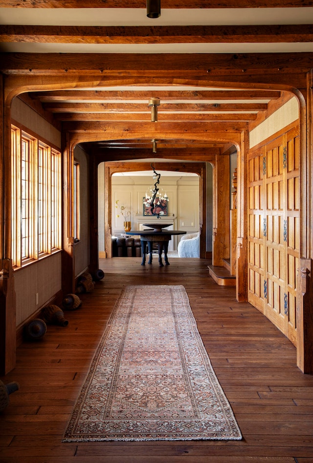 hall featuring beamed ceiling, dark wood-type flooring, and an inviting chandelier