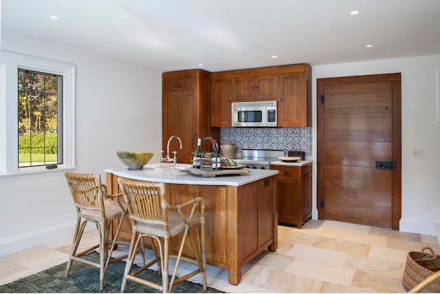 kitchen featuring a kitchen bar, backsplash, stainless steel appliances, a kitchen island with sink, and sink