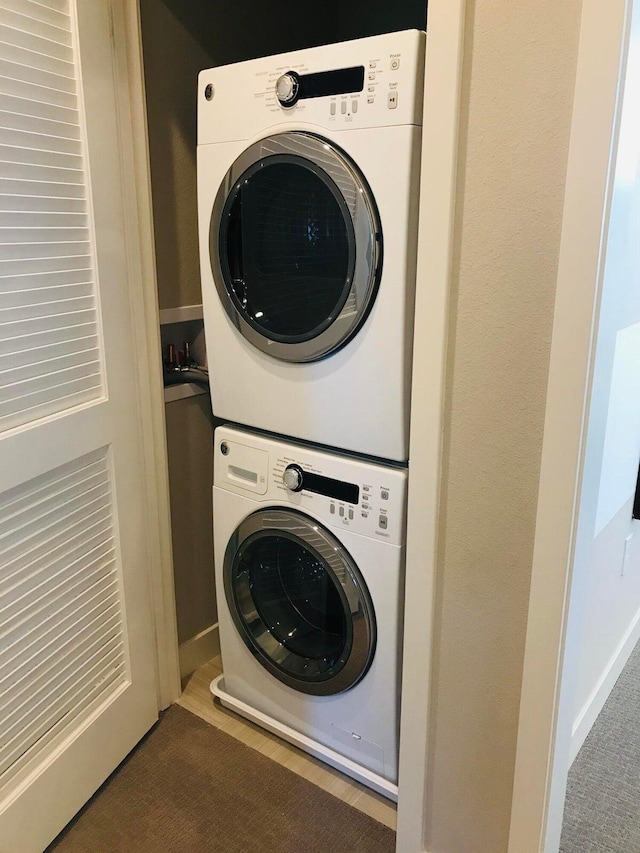 clothes washing area featuring dark colored carpet and stacked washing maching and dryer