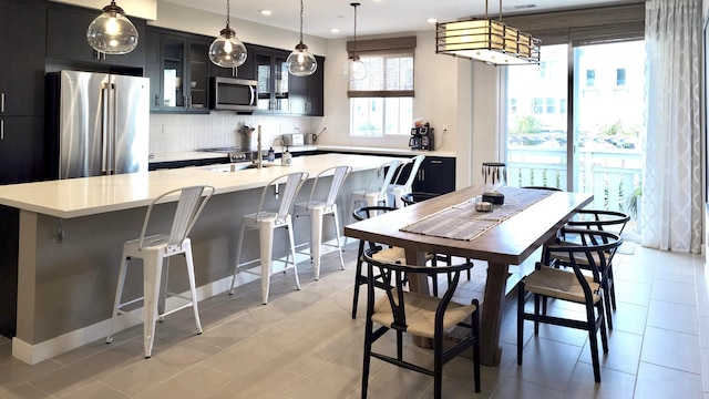 kitchen with hanging light fixtures, appliances with stainless steel finishes, a kitchen bar, and a kitchen island with sink