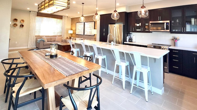 kitchen with stainless steel appliances, sink, decorative light fixtures, a center island with sink, and a breakfast bar area