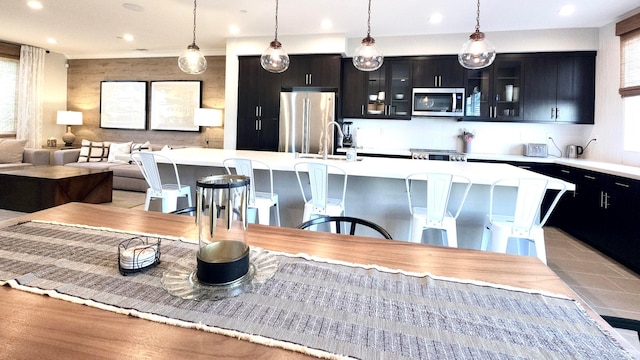 kitchen featuring stainless steel appliances, a healthy amount of sunlight, hanging light fixtures, a breakfast bar area, and an island with sink