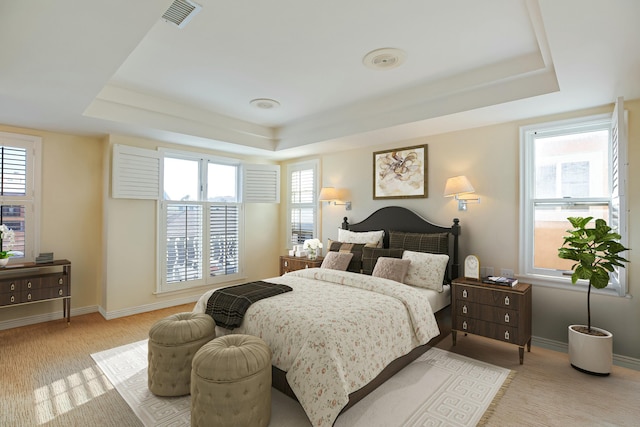 bedroom with a raised ceiling, multiple windows, and light colored carpet