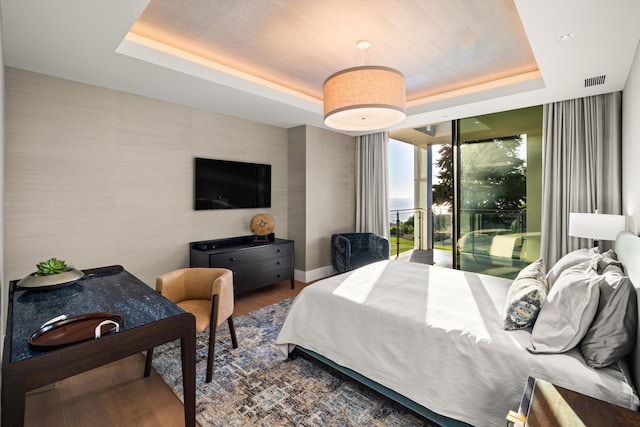 bedroom featuring a tray ceiling, expansive windows, and hardwood / wood-style flooring