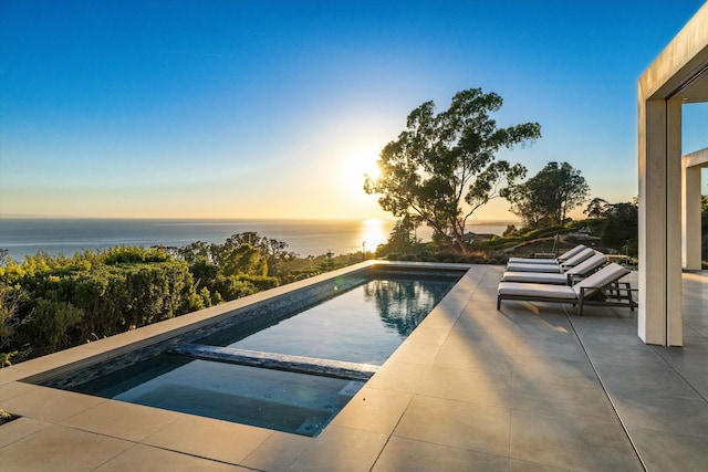 pool at dusk with a water view and an in ground hot tub