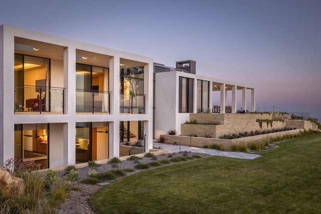 back house at dusk with a lawn and a balcony