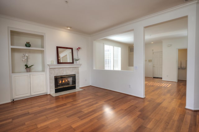 unfurnished living room with built in shelves, crown molding, a high end fireplace, and dark wood-type flooring