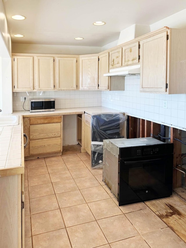 kitchen featuring backsplash, black range oven, sink, light tile patterned floors, and light brown cabinetry