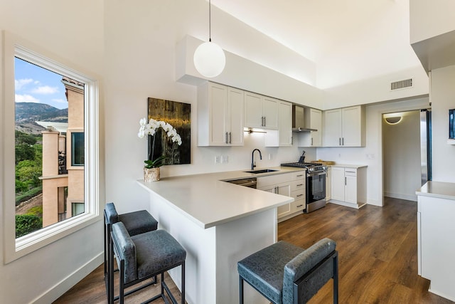 kitchen with wall chimney range hood, kitchen peninsula, decorative light fixtures, a kitchen bar, and stainless steel range with gas stovetop