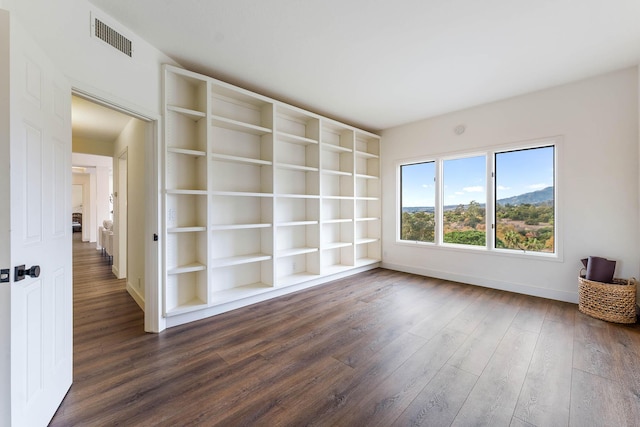 empty room featuring built in shelves and dark hardwood / wood-style floors