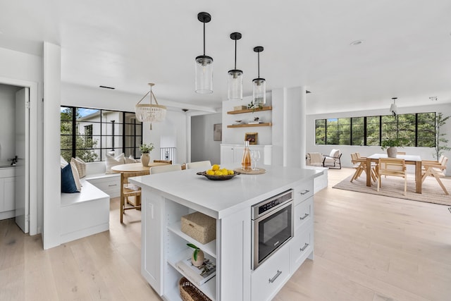 kitchen featuring light wood-type flooring, decorative light fixtures, a notable chandelier, white cabinets, and a kitchen island