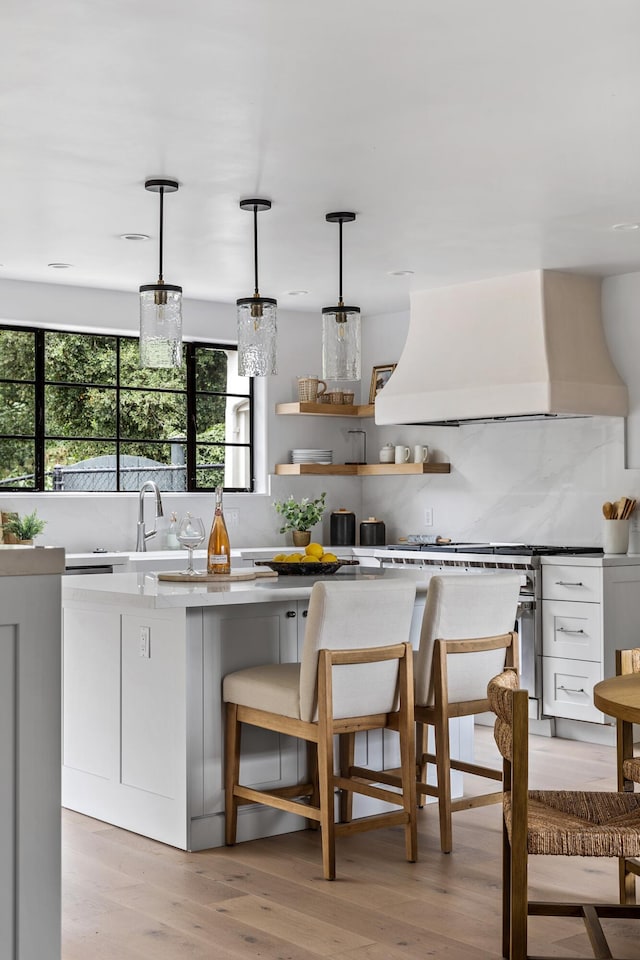 kitchen featuring hanging light fixtures, light hardwood / wood-style flooring, custom range hood, tasteful backsplash, and white cabinetry