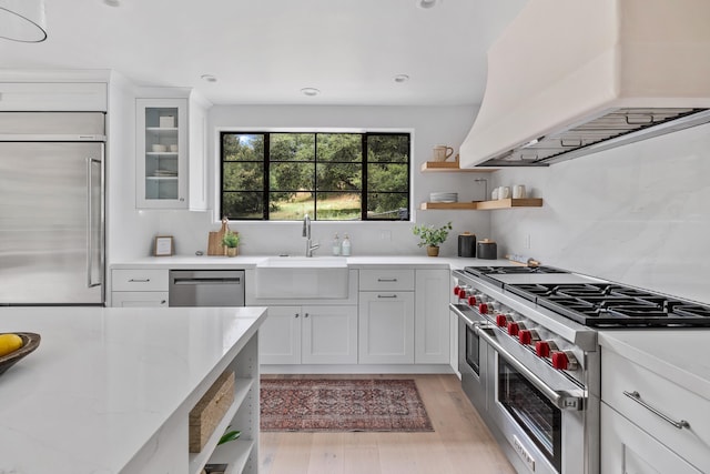 kitchen featuring light stone countertops, custom range hood, white cabinetry, and high quality appliances