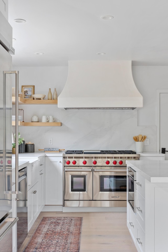 kitchen with stainless steel appliances, premium range hood, backsplash, light hardwood / wood-style floors, and white cabinets