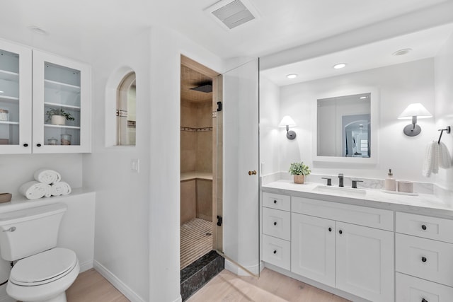 bathroom with hardwood / wood-style flooring, vanity, toilet, and a tile shower