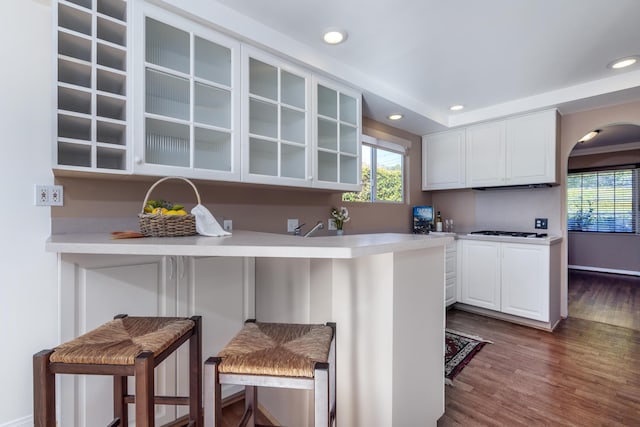 kitchen featuring a kitchen bar, white cabinets, kitchen peninsula, and dark wood-type flooring