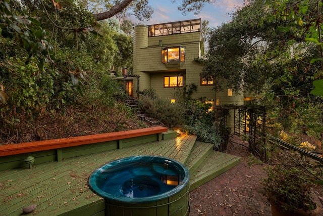 back house at dusk with an outdoor bar, a hot tub, and a wooden deck