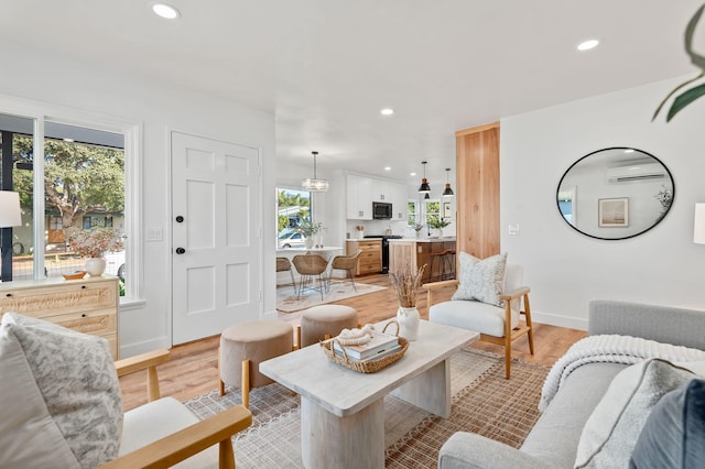 living room featuring light hardwood / wood-style flooring, a wealth of natural light, and an AC wall unit