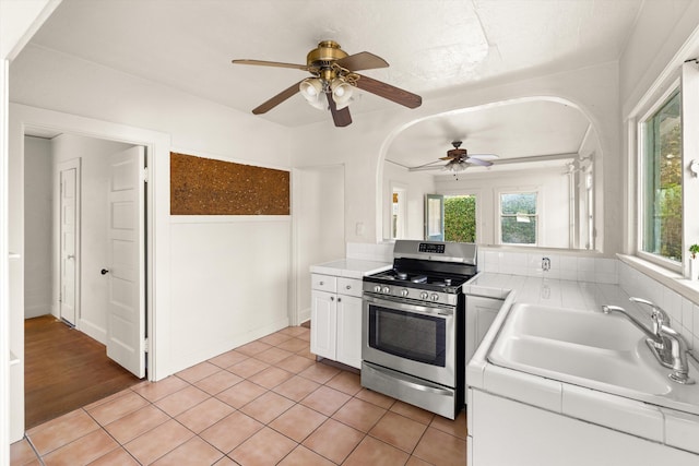 kitchen with stainless steel gas range oven, ceiling fan, sink, light tile patterned floors, and white cabinets