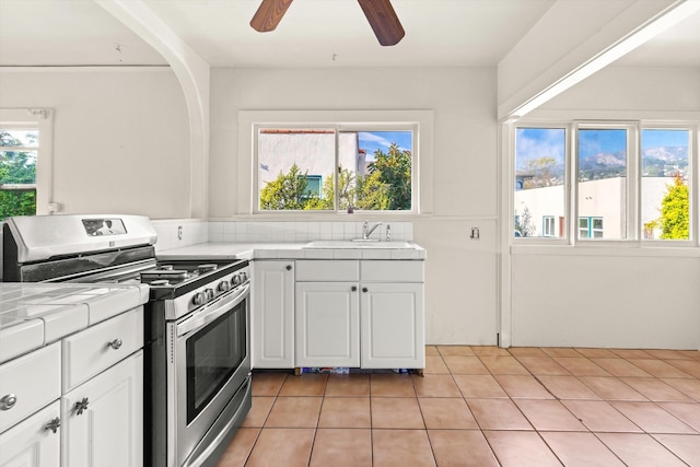 kitchen featuring tile countertops, white cabinets, sink, and gas range