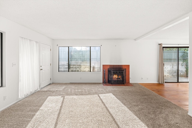 unfurnished living room featuring beam ceiling, hardwood / wood-style flooring, a wealth of natural light, and a tiled fireplace