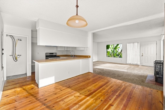 kitchen with kitchen peninsula, sink, pendant lighting, stainless steel gas stove, and light hardwood / wood-style floors