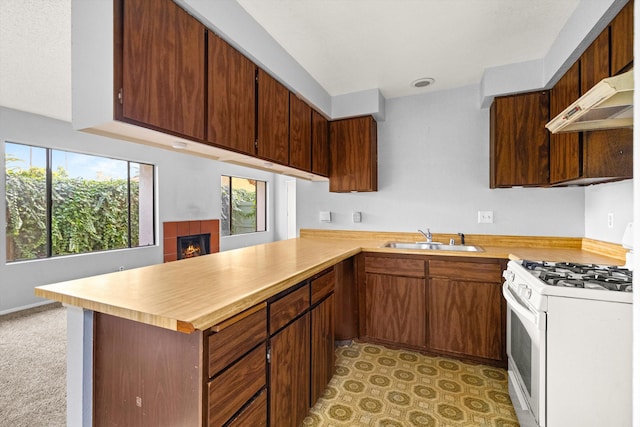 kitchen featuring kitchen peninsula, sink, white range with gas stovetop, and a tile fireplace