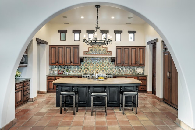 kitchen featuring wood counters, an inviting chandelier, a center island with sink, tasteful backsplash, and decorative light fixtures