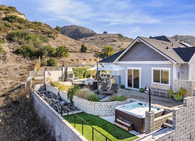 rear view of property with an outdoor living space with a fireplace, a mountain view, a patio area, and a hot tub