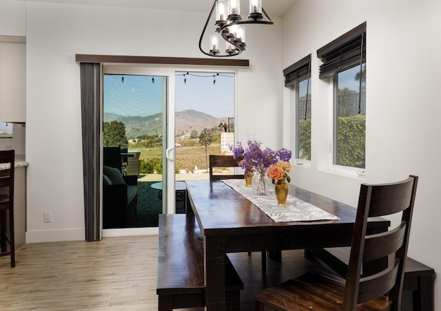 dining room with a mountain view, light hardwood / wood-style flooring, a healthy amount of sunlight, and an inviting chandelier