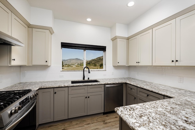 kitchen with sink, light stone counters, decorative backsplash, appliances with stainless steel finishes, and hardwood / wood-style flooring