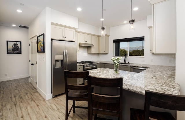 kitchen featuring pendant lighting, sink, light wood-type flooring, appliances with stainless steel finishes, and light stone counters