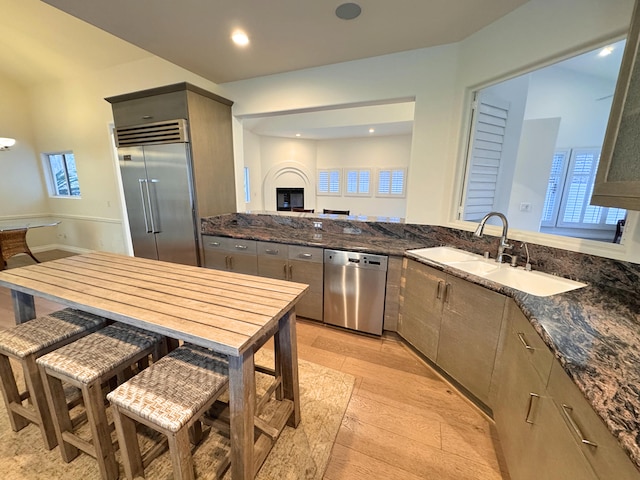 kitchen featuring sink, gray cabinets, dark stone countertops, light hardwood / wood-style floors, and stainless steel appliances