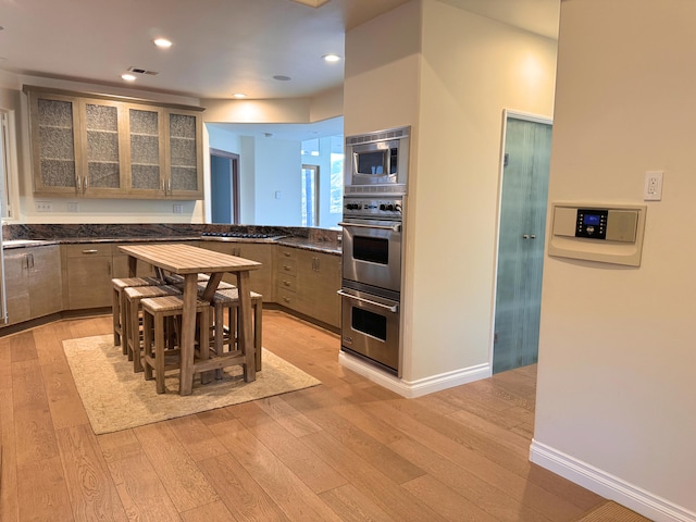 kitchen featuring appliances with stainless steel finishes, light brown cabinetry, light hardwood / wood-style floors, and a breakfast bar area