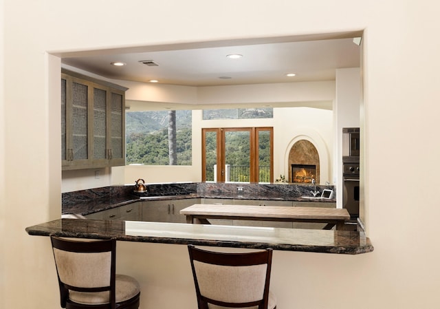 bar featuring dark stone counters, oven, sink, a fireplace, and gas cooktop